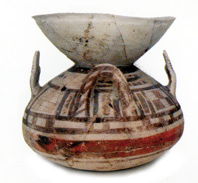 <i>Olla</i> con labbro ad imbuto, alta cm 28. Ha due anse e due prese a forma di mano. Decorazione anche a scacchi. Repe