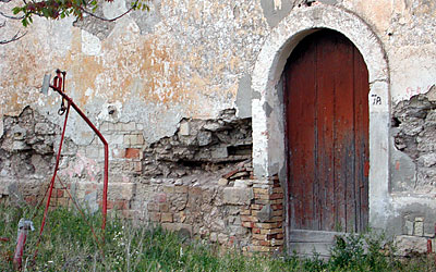 Facciata laterale. Uno degli ingressi con porta in legno e, in basso a destra un piccolo foro per la libera uscita del g